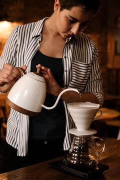 Female professional barista pouring hot water from kettle in V60 funnel