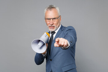 Displeased elderly gray-haired business man in classic blue suit shirt tie isolated on grey background. Achievement career wealth business concept. Hold megaphone, pointing index finger on camera.