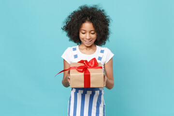 Excited little african american kid girl 12-13 years old in striped clothes isolated on blue...