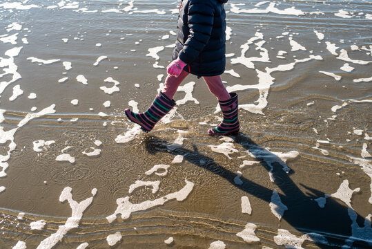 Girl walking in gumboots at the beach, New Zealand.