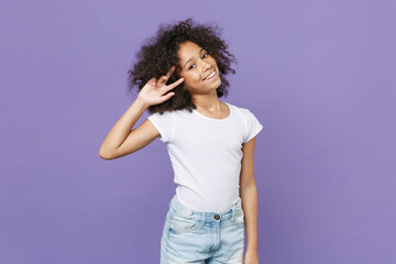 Smiling little african american kid girl 12-13 years old in white t-shirt isolated on pastel violet background studio portrait. Childhood lifestyle concept. Mock up copy space. Showing victory sign.
