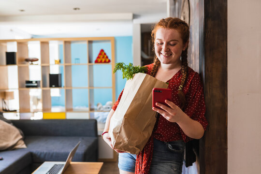Happy red haired woman looking at her phone inside the house