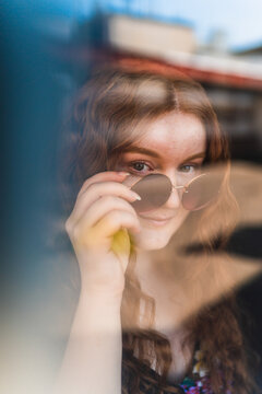 Red hair woman behind a closed window taking off her sunglasses
