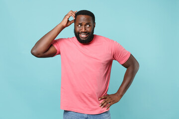 Puzzled young african american man guy in casual pink t-shirt posing isolated on pastel blue background studio portrait. People lifestyle concept. Mock up copy space. Put hand on head, looking aside.