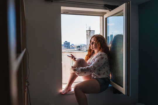 Beautiful Long Red Haired Girl, Sitting On A Window