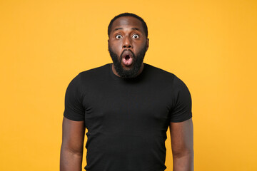 Shocked african american man guy football fan in casual black t-shirt isolated on yellow background...
