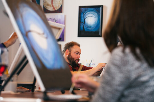 Painting: Man Works On Artwork With Others In Class