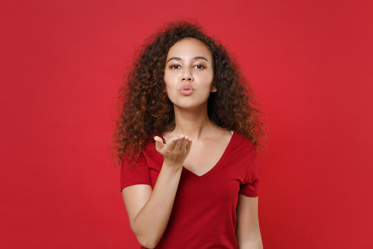 Charming young african american woman girl in casual t-shirt posing isolated on red background studio portrait. People sincere emotions lifestyle concept. Mock up copy space. Blowing sending air kiss.