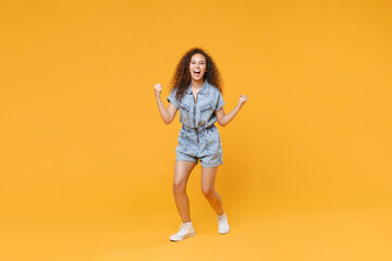 Fototapeta na wymiar Full length portrait of joyful young african american woman girl in denim clothes isolated on yellow background studio portrait. People lifestyle concept. Mock up copy space. Doing winner gesture.
