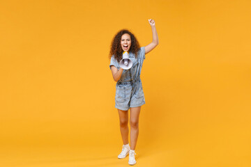 Fototapeta na wymiar Full length portrait of crazy young african american woman girl in denim clothes isolated on yellow wall background studio portrait. People lifestyle concept. Screaming on megaphone, clenching fist.