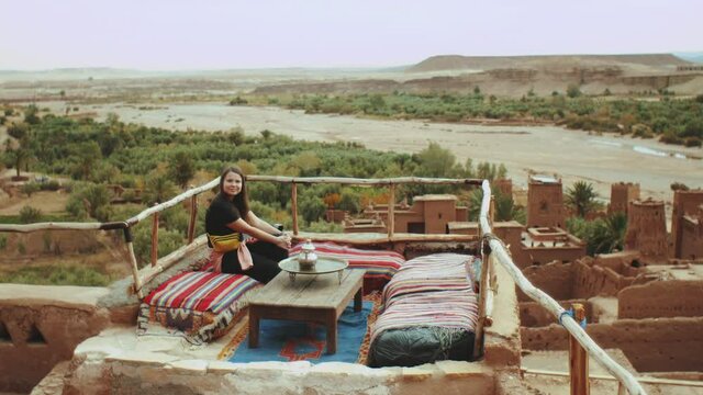 Pretty woman sitting on a rooftop terrace with a beautiful view of the ruins of an abandoned city The famous Ait Benhaddou Kasbah, old town, Beautiful touristic places of Morocco, full hd