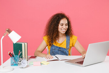 Smiling young african american girl employee in office sit at desk work on laptop pc computer...