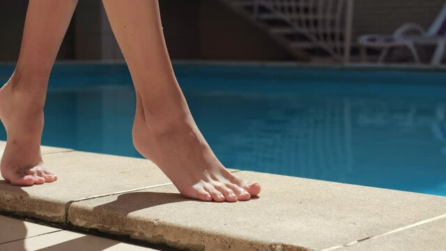 Close up view of slim female tanning barefoot legs careful walking on poolside in spa resort. Woman stepping near pool water tough ground by wet toes, summer relaxation and joy in spa abroad