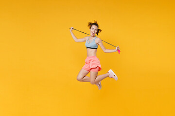 Fototapeta na wymiar Full length portrait excited young fitness woman in sportswear working out isolated on yellow background. Workout sport motivation lifestyle concept. Mock up copy space. Jumping, hold skipping rope.