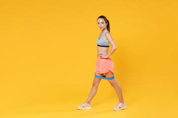 Full length portrait of young fitness sporty woman girl in sportswear working out isolated on yellow background. Workout sport motivation lifestyle concept. Doing exercise for legs with fitness gums.