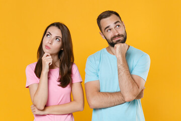 Puzzled young couple two friends guy girl in blue pink t-shirts isolated on yellow background studio portrait. People lifestyle concept. Mock up copy space. Put hands prop up on chins, looking up.