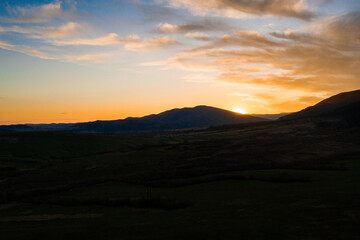 Carpathian meadow and beautiful sunset in the mountains - spring landscape, spruces on the hills, dark cloudy sky and bright sunlight, the village can be seen on the horizon.