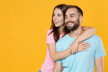 Smiling young couple friends guy girl in blue pink t-shirts posing isolated on yellow wall background studio portrait. People emotions lifestyle concept. Mock up copy space. Hugging, looking aside.