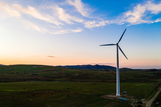 Wind turbine, alternative energy, wind energy, one windmill in a field in the mountains, top view of a wind turbine at sunset. - Powered by Adobe