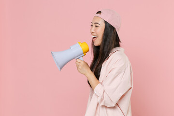 Side view of funny young asian woman girl in casual clothes cap posing isolated on pastel pink background studio. People lifestyle concept. Mock up copy space. Screaming in megaphone, looking aside.