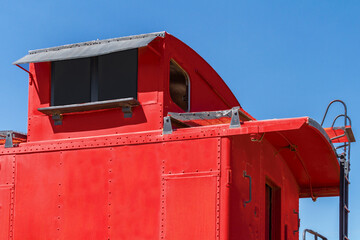 A top position of a vintage red railroad caboose with a clear blue sky