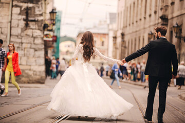 Happy newlyweds couple on a walk in old European town street, gorgeous bride in white wedding dress...