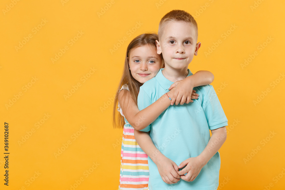 Wall mural Little couple kids boy girl 5-6 years old in blue pink clothes shirt dress posing have fun isolated on yellow background children studio portrait. People childhood lifestyle concept embrace hug love