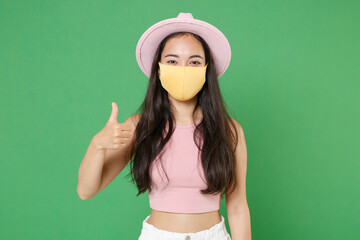 Young asian woman girl in casual pink clothes hat yellow face mask isolated on green wall...