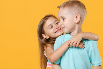 Little couple kids boy girl 5-6 years old in blue pink clothes shirt dress posing have fun isolated on yellow background children studio portrait. People childhood lifestyle concept embrace hug love