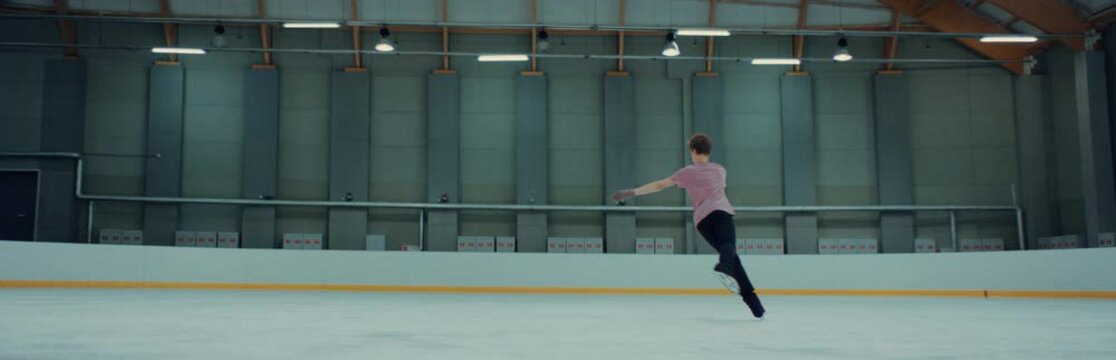 Young teenager male ice figure skater falls on ice while practicing jumps on the rink. Shot on RED cinema camera with 2x Anamorphic lens, 75 FPS slow motion