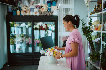 Young attractive brunette caucasian woman florist in a pink dress arranging a bouquet of flowers in...