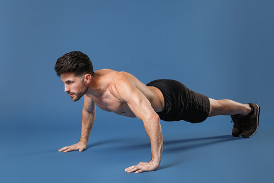 Full length portrait of young fitness sporty strong guy bare-chested muscular sportsman isolated on blue background. Workout sport motivation lifestyle concept. Doing push-ups exercises looking aside.