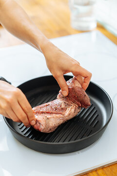 Woman placing steak in spices on grill pan on stove