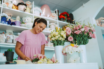 Young attractive brunette caucasian woman florist in a pink dress arranging a bouquet of flowers in a flower shop