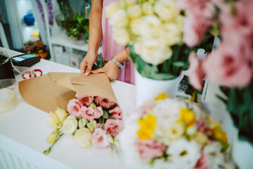 Closeup of hands of a caucasian woman in a pink dress arranging a bouquet of flowers on a table in a flower shop. Making a bouquet of flowers