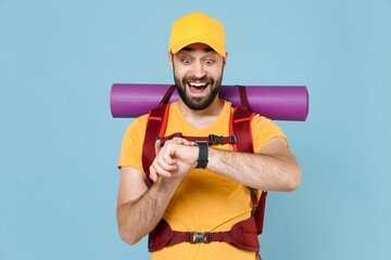 Surprised traveler young man in yellow casual t-shirt cap with backpack isolated on blue wall background. Tourist traveling on weekend getaway. Tourism discovering hiking concept. Wearing smart watch.