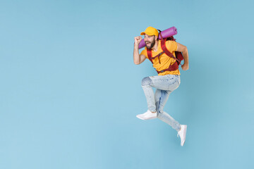 Full length portrait Excited young traveler man in cap with backpack isolated on blue wall background. Tourist traveling on weekend getaway. Tourism discovering hiking concept. Jumping like running.
