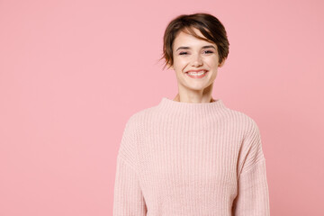 Smiling beautiful young brunette woman girl wearing knitted casual sweater posing isolated on pastel pink wall background studio portrait. People sincere emotions lifestyle concept. Looking camera.