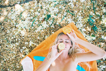 blonde woman on colorful beach towel with oranges and lemons on eyes or hiding eyes in summer in 1980s colors