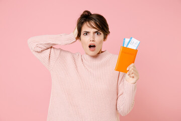 Shocked worried woman in casual sweater isolated on pastel pink background. Passenger traveling abroad to travel on weekends getaway. Air flight journey concept. Hold passport ticket put hand on head.