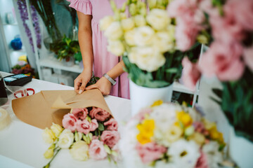 Closeup of hands of a caucasian woman in a pink dress arranging a bouquet of flowers on a table in a flower shop. Making a bouquet of flowers