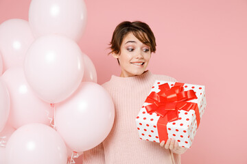 Excited young woman in knitted casual sweater isolated on pastel pink background. Birthday holiday party people emotions concept. Celebrating hold air balloons red present box with gift ribbon bow.