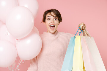 Excited young woman girl in casual sweater isolated on pastel pink background. Birthday holiday party people emotions concept. Celebrating hold air balloons package bag with purchases after shopping.