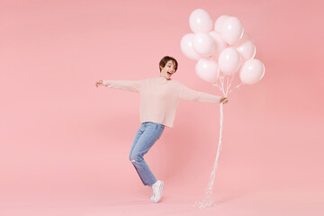 Fototapeta na wymiar Full length portrait of excited young woman girl in casual sweater isolated on pink background. Birthday holiday party concept. Celebrating hold air balloons dancing standing on toes spreading hands.