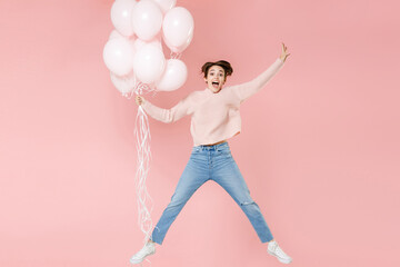 Full length portrait of surprised young woman in casual sweater isolated on pink background. Birthday holiday party people emotions concept. Celebrating hold air balloons jumping spreading hands legs.