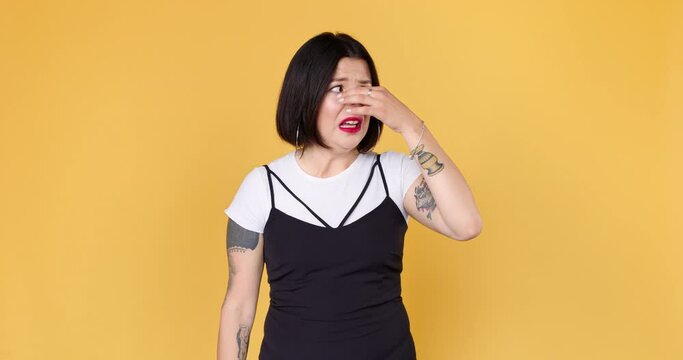 Repulsion to bad smell. Unhappy woman with tattoo squeezing nose with fingers, smells something awful. Spoiled air.