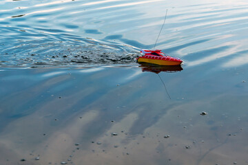 A toy radio-controlled boat floats in the lake.