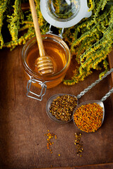 Honey in a glass jar with a wooden spoon. Still life on a wooden table with yellow flowers Goldenrod. Healthy sweet food. Close up with selective focus.