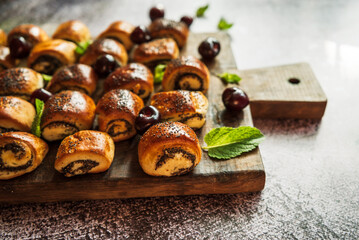 small buns with poppy seeds with cherries and mint leaves on a brown wooden board on a gray background 3