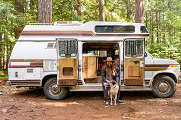A young man posing with his dog outside of a camper van